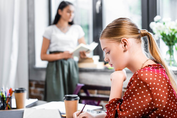 selective focus of blonde student in blouse writing with pencil