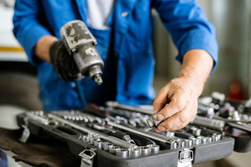 Mature technician or repairman taking one of iron nozzles for technical drill