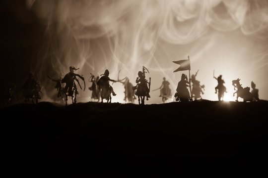 Medieval battle scene with cavalry and infantry. Silhouettes of figures as separate objects, fight between warriors on dark toned foggy background. Night scene.