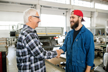 Happy young bearded repairman of maintenance service greeting mature client