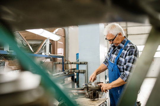 Aged grey-haired master of repair service fixing engine parts with wrench