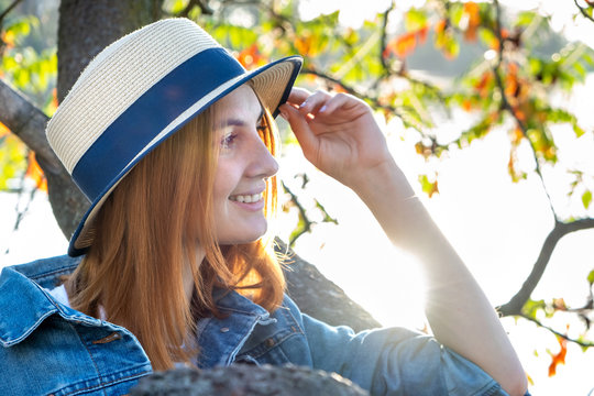 Portrait of gorgeous smiling teenage girl in yellow hat and with red hair wearing geans jacket outdoors on sunny autumn day.