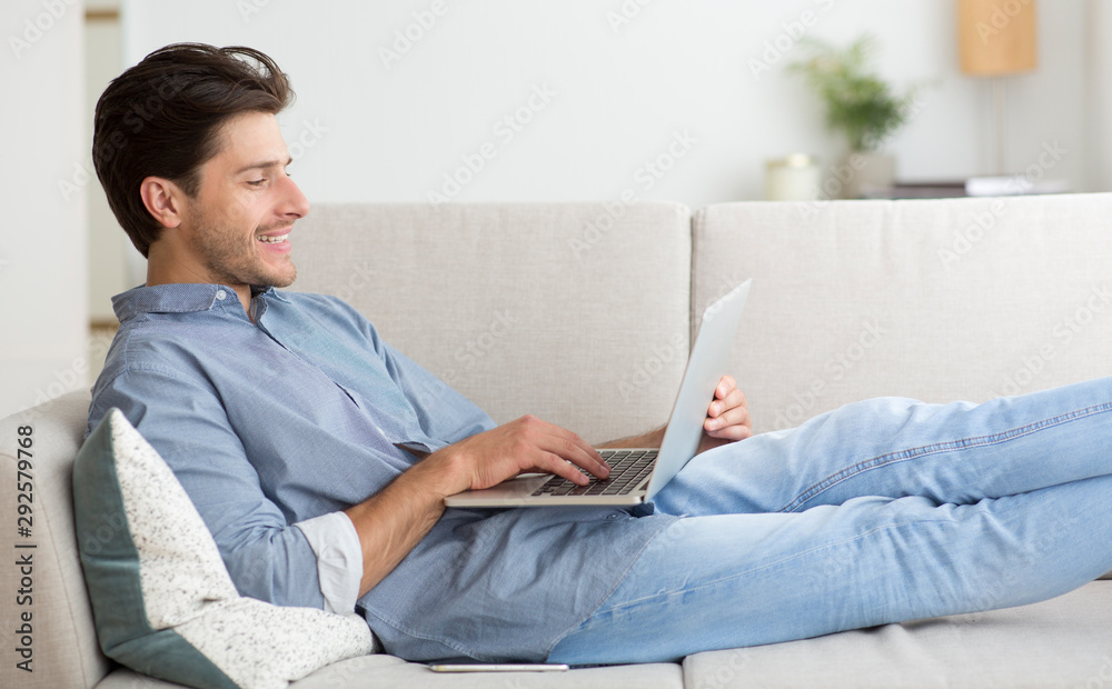 Poster Guy Working On Laptop Computer Lying On Sofa At Home