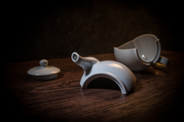 broken teapot on a dark toned foggy background. Pieces of ceramic teapot on wooden table.