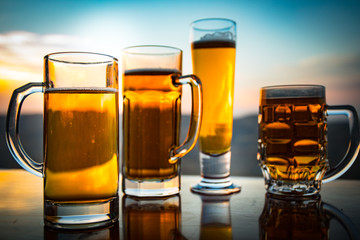 Glass of beer on a beach at sunset. Cooling summer drink concept. Close Up of A Glass of Draught Beer with the Bokeh of Sunlight Background