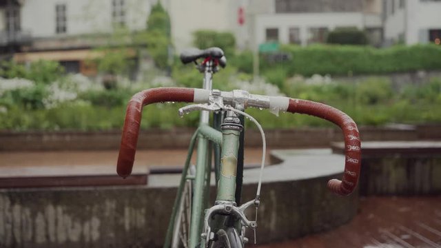 Wet handlebars with brown handles and bike seat on a rainy day. Close up