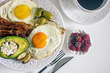 Keto Diet LCHF Keto breakfast. Fried eggs with bacon, avocado, cream cheese, nuts, olives and coffee on a white plate on a light background. Low carb diet concept. high fat diet. Keto bacon and eggs 