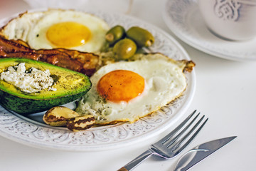 Keto Diet LCHF Keto breakfast. Fried eggs with bacon, avocado, cream cheese, nuts, olives and coffee on a white plate on a light background. Low carb diet concept. high fat diet. Keto bacon and eggs 