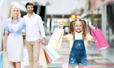 Parents And Excited Daughter Carrying Shopping Bags Walking In Mall