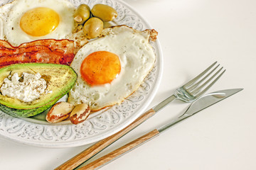 Keto Diet LCHF Keto breakfast. Fried eggs with bacon, avocado, cream cheese, nuts, olives and coffee on a white plate on a light background. Low carb diet concept. high fat diet. Keto bacon and eggs 