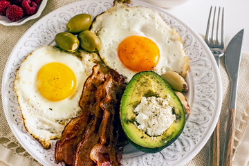 Keto Diet LCHF Keto breakfast. Fried eggs with bacon, avocado, cream cheese, nuts, olives and coffee on a white plate on a light background. Low carb diet concept. high fat diet. Keto bacon and eggs 