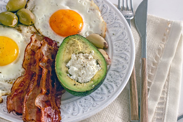 Keto Diet LCHF Keto breakfast. Fried eggs with bacon, avocado, cream cheese, nuts, olives and coffee on a white plate on a light background. Low carb diet concept. high fat diet. Keto bacon and eggs 