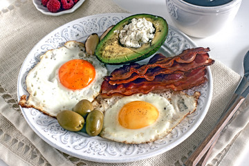Keto Diet LCHF Keto breakfast. Fried eggs with bacon, avocado, cream cheese, nuts, olives and coffee on a white plate on a light background. Low carb diet concept. high fat diet. Keto bacon and eggs 