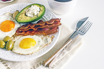 Keto Diet LCHF Keto breakfast. Fried eggs with bacon, avocado, cream cheese, nuts, olives and coffee on a white plate on a light background. Low carb diet concept. high fat diet. Keto bacon and eggs 