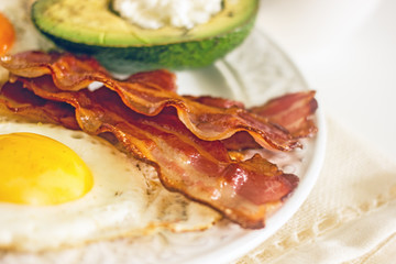 Keto Diet LCHF Keto breakfast. Fried eggs with bacon, avocado, cream cheese, nuts, olives and coffee on a white plate on a light background. Low carb diet concept. high fat diet. Keto bacon and eggs 