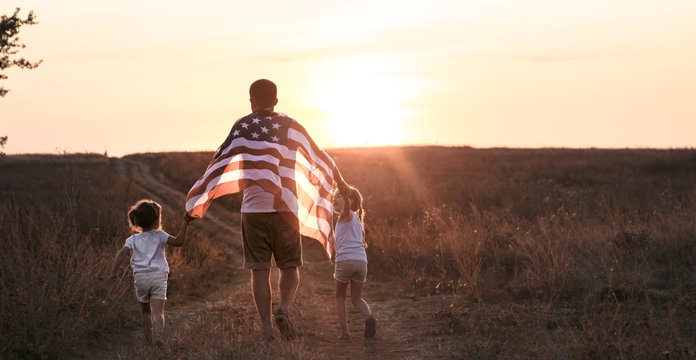 A Happy Family With An American Flag At Sunset.