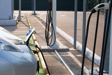 Ecology friendly transport concept. Loading energy. Gray car is charged on electric charging station in parking. Electricity and automobile.