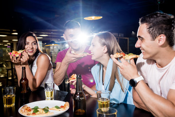 Cheerful friends in the pub. Drinking beer, eating pizza, talking, having fun.