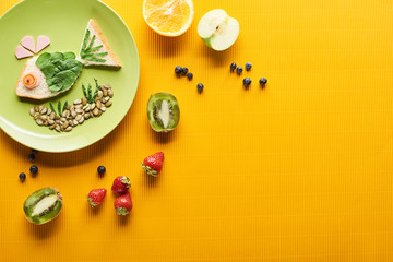 top view of plate with fancy fish made of food near scattered fruits on colorful orange background