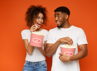 Positive african man and woman eating popcorn - obrazy, fototapety, plakaty