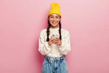 Smiling pretty millennial girl uses modern mobile phone, connected to wireless internet, downloads...