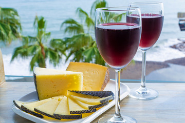 Red wine served in glasses with spanish cheese in lounge bar with sea view and palm trees