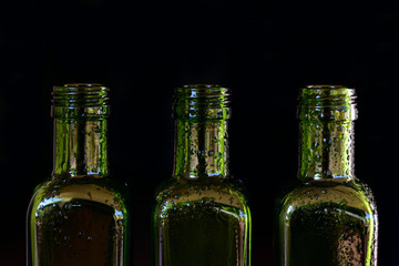three green glass bottles with drops of water stand side by side against a dark background