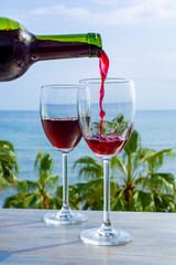 Waiter pouring red wine in glasses in lounge bar with sea view and palm trees