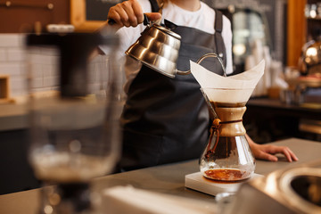 Professional barista preparing coffee using chemex pour over coffee maker and drip kettle. Young woman making coffee. Alternative ways of brewing coffee. Coffee shop concept. - obrazy, fototapety, plakaty