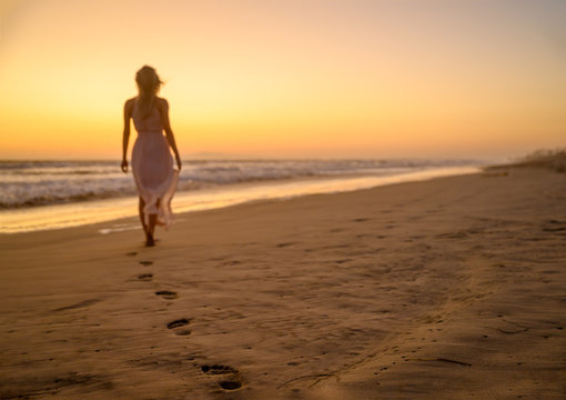 Beautiful woman wearing a gorgeous summer clothes and walking away into the sunset somewhere on the southern coast of the Pacific Ocean