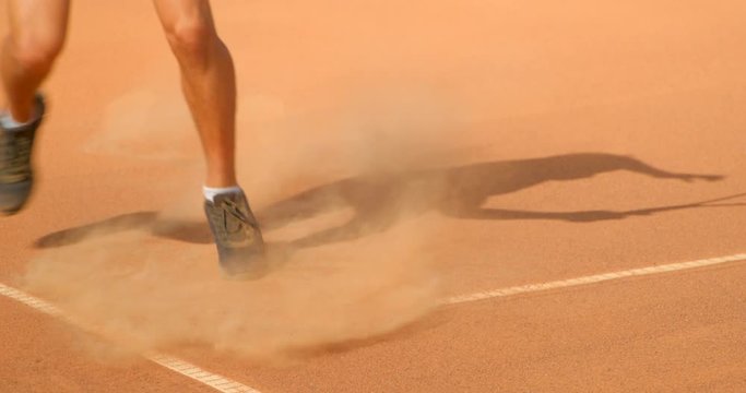 Close up tennis action on a clay court of a player sliding in to play a shot in slow motion.