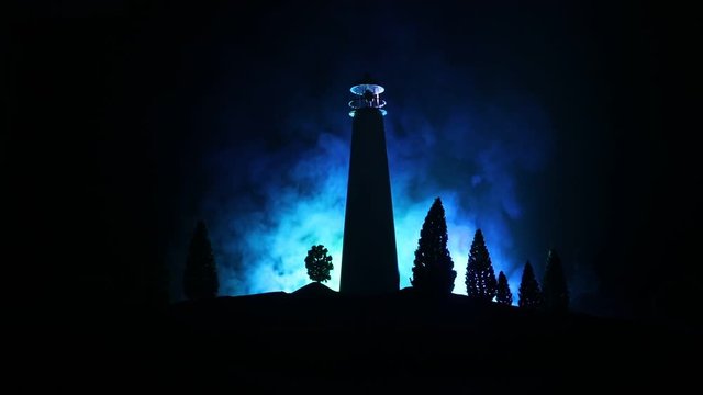 Lighthouse with light beam at night with fog. Old lighthouse standing on mountain. Table decoration. Toned background. Moonlighting. Selective focus