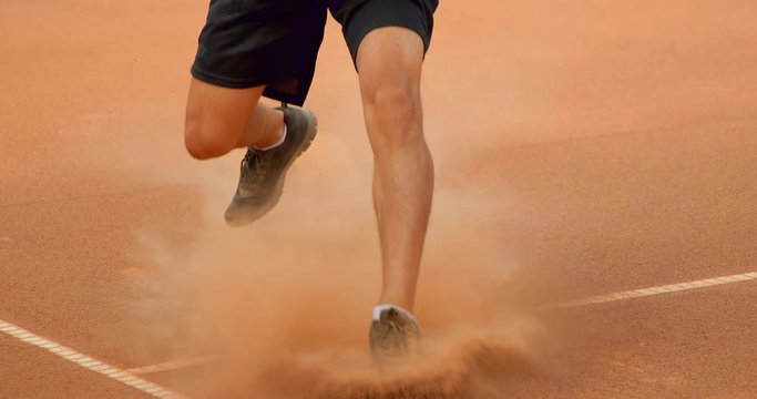A Tennis Player sprints in and slides to play a shot in slow motion of a clay court.