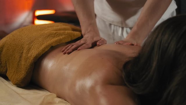 Body relaxation and skin care. Close-up of woman enjoying back massage at spa club in beautiful ambient light. Female relaxing lying on massage table. 4k, UHD
