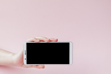 Modern mobile phone in a woman's hand on pink background