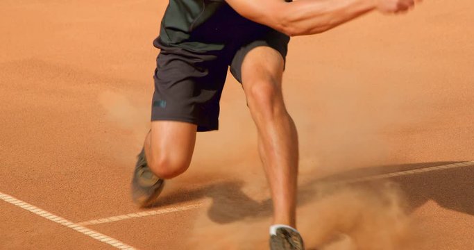 A Tennis player sprints across a clay tennis court to playa shot in slow motion.
