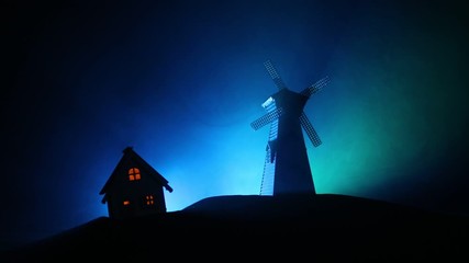 Windmill silhouette standing on hill against the night sky. Night decor with old windmill on hill with horror toned foggy background with light. Horror concept