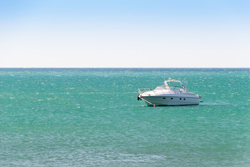 White boat anchored in a turquoise water of sea bay. Skyline and clear sky in frame. Vacation at sea.