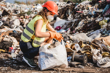 Woman volunteer helps clean the field of plastic garbage. Bushes and sky in the background. Earth day and ecology.