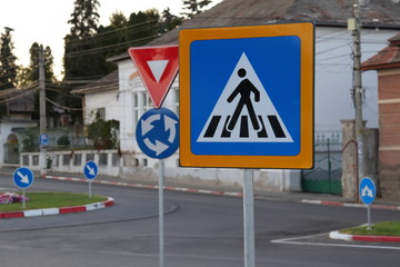 multiple street signs in a roundabout, pedestrian crossing, right of way