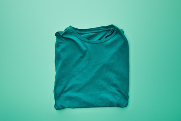 top view of blank color folded t-shirt on turquoise background