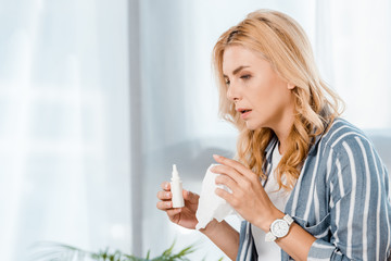 sick woman holding nasal spray and napkin at home