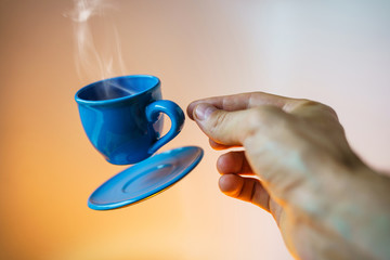 Floating blue cup of espresso with hands. First-person view. Mock up of soaring in the air cup of hot coffee. Levitate concept