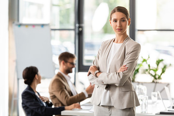 attractive businesswoman in formal wear standing with crossed arms in office