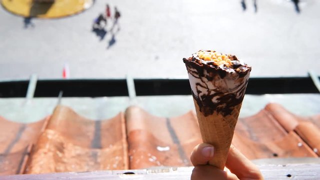 Hand holding twirling one white vanilla chocolate swirl ice cream gelato cone with peanuts bokeh background of people walking in Warsaw Old Town