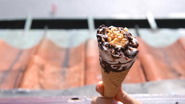 Hand holding twirling one white vanilla chocolate swirl ice cream gelato cone with peanuts in slow motion in Warsaw Old Town
