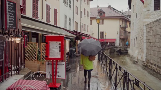 Woman in yellow coat walk by old european streets in rainy weather with black polka-dot umbrella