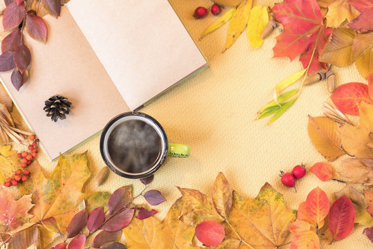 Autumn mudboard concept: a cup of hot coffee, a revealed notebook with clean pages. Frame of Scattered seasonal yellow and red leaves. Flat lay. Copy space