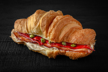 Croissant sandwich with bacon, baked pepper, capers. Healthy, tasty, nourishing snack. Take away food