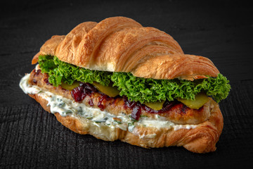 Croissant sandwich with grilled sausages, pickles, lettuce, tar tar sauce. Healthy, tasty, nourishing snack. Take away food